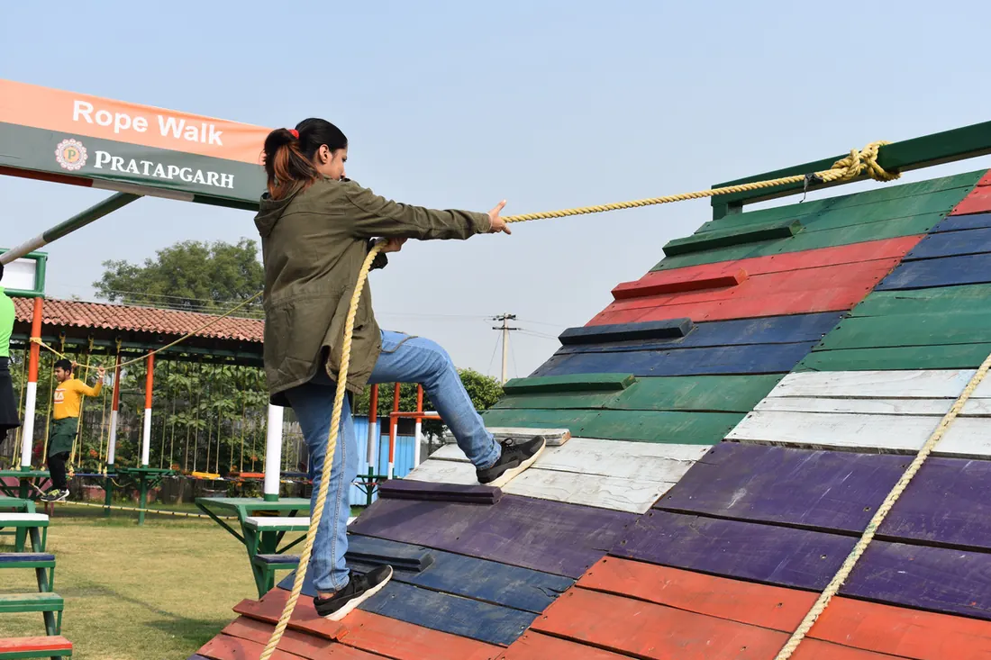 Woman gripping ropes as she climbs a slanted wall of colourful planks at the rope walk