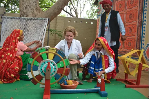 Women in traditional dress showing a visitor how to spin yarn on a rainbow-painted charkha