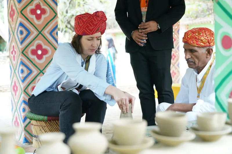 Woman in a red turban shaping wet clay beside an artisan, rows of new pots in front