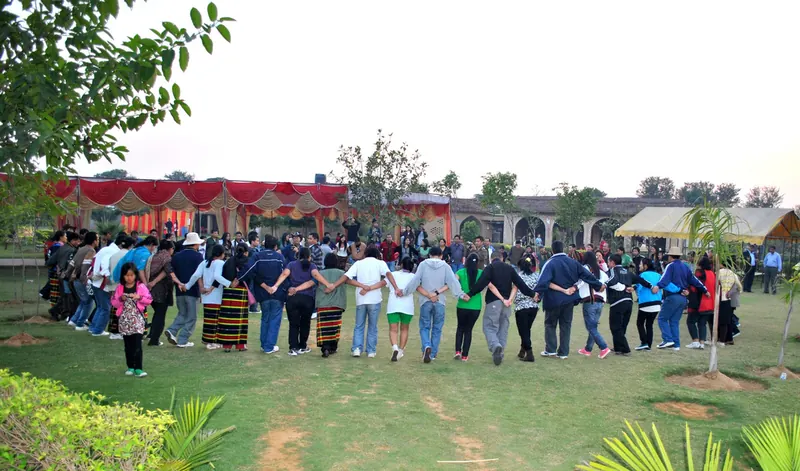 Large group standing in a hand-holding circle on the lawn before a red-draped pavilion