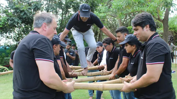 Team in black polos holding bamboo poles steady as a colleague balances across them