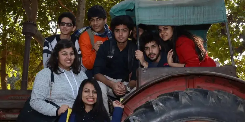 Group of young visitors posing on a red tractor with a green canopy under trees