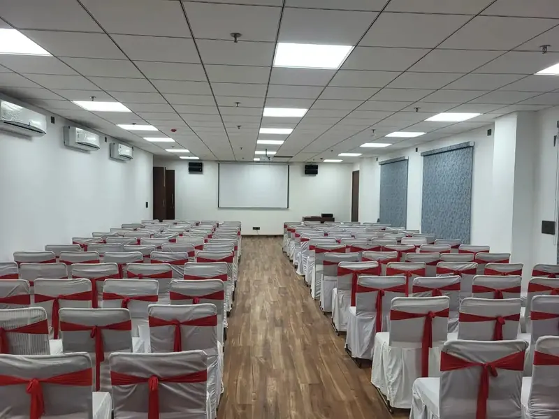 Empty conference hall with projector screen and rows of chairs in red sashes