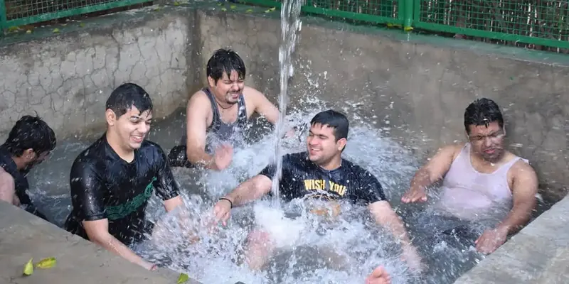 Men in a water pool laughing and splashing as a hose sprays