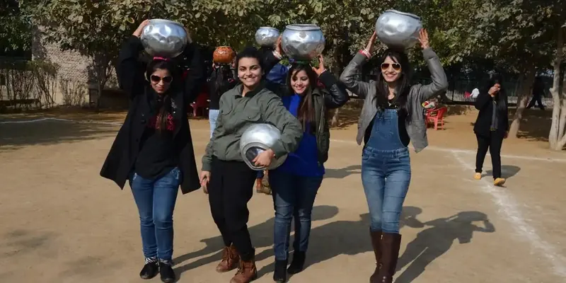 Women posing outdoors with steel buckets balanced on their heads