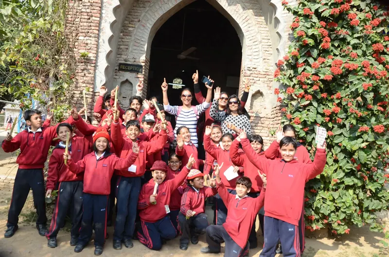 Children in red tracksuits waving wooden sticks and cheering outside a brick archway