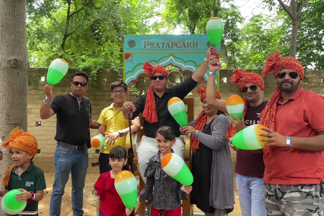 A family group in orange turbans and sunglasses holding green and orange balloons before the painted Pratapgarh gate