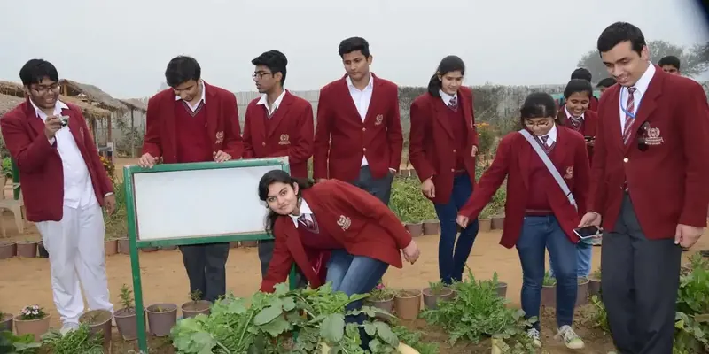 Children in maroon blazers examining potted plants beside a white board in the farm's nursery